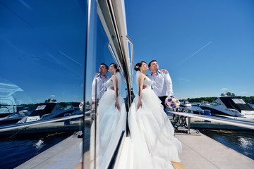 Wedding couple is hugging on a yacht. Beauty bride with groom. Beautiful model girl in white dress. Man in suit. Female and male portrait. Woman with lace veil. Cute lady and guy outdoors