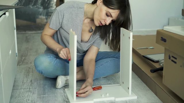 Young woman assembling furniture with screwdriver in her new home, 4K
