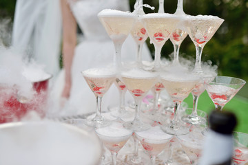 Beautiful wedding couple is pouring champagne indoors. Colorful glasses for alcohol with berries for bride and groom. Beauty of bridal interior for marriage. Bright bar for celebration