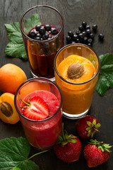 Fresh strawberry, blueberry and apricot smoothies on black wooden background. Selective focus