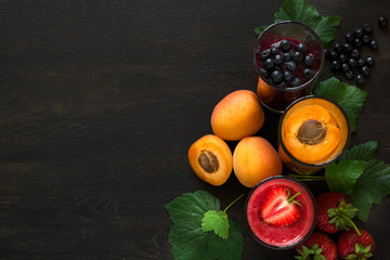 Fresh strawberry, blueberry and apricot smoothies on black wooden background. Selective focus