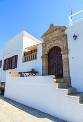 Beautiful large wooden door, surrounded by marble and a typical house on the island of Lindos.
