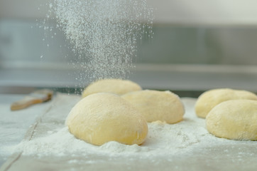 Delicious bread dough buns sitting on metal surface with flour being sprinkled as topping before baking