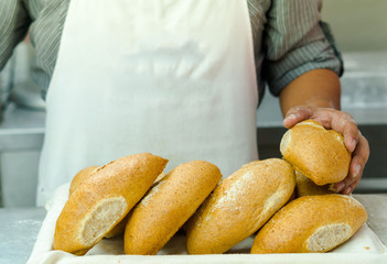 Pile of fresh bread loafs, baker standing behind with only apren and arms visible, bakery concept