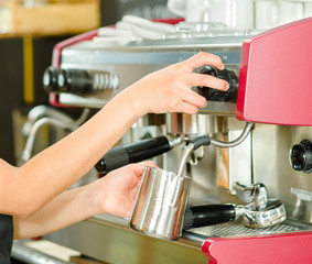 Female hands working operating industrial coffee maker, steaming milk in metal container