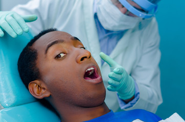 Young hispanic male lying in dental chair and looking nervously into camera, dentists facial mask...
