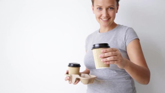 Follow focus changes from backround to front, smiling young woman presents paper cup on camera