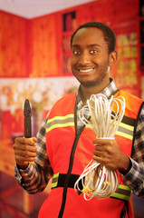 Young electrical worker wearing safety vest, holding cables and cable pliars, smiling with great...