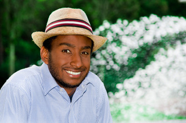 Good Looking man wearing blue shirt and summer hat smiling while enjoying beautiful day in park environment