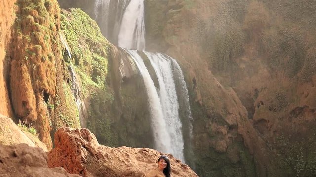 Happy woman waving with hand with waterfall background. Filmed in Morocco , Ouzoud waterfall - slow motion