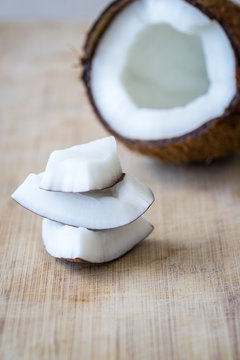 Vertical view of a cracked coconut on rustic wooden table background. Small pieces of coconut in foreground.