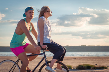 Young woman and man riding a bicycle at the shore