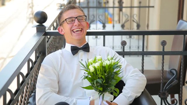 Young man is sitting with wedding bouquet on the balcony and speaking