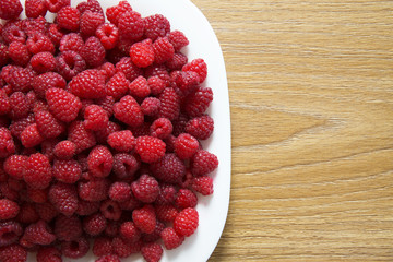 Fresh raspberries in a white plate on a wooden table