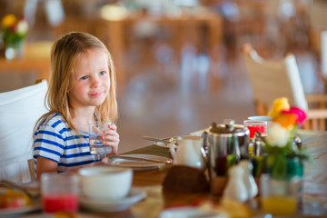 Little kid having breakfast at outdoor cafe. Adorable girl drinking fresh watermelon juice enjoying breakfast.