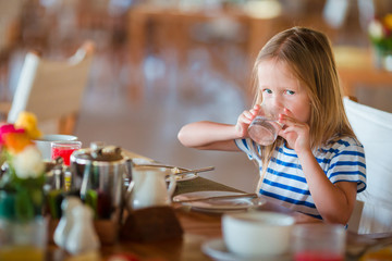 Little kid having breakfast at outdoor cafe. Adorable girl drinking fresh watermelon juice enjoying breakfast.