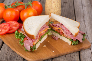 Roast Beef and Cheese Sandwich With Tomatoes and Mustard in Background