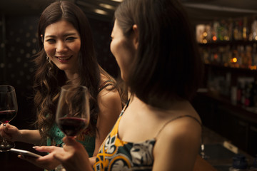 Young women looking at a smart phone with a glass of wine at the bar