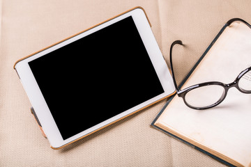 Reading table with tablet PC and old book and eyeglasses