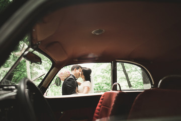 Beautiful wedding couple posing near splendid retro car