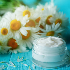 Fototapeta na wymiar Cosmetic cream with camomile flower for a body and face on blue