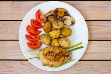 fried chicken fillet with potatoes tomatoes and mushrooms. on a wooden background
