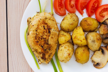 fried chicken fillet with potatoes tomatoes and mushrooms. on a wooden background