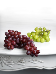Red and white bunches of grapes on white table.