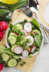 Salad with spinach, cucumber, radish in a bowl on a white backgr