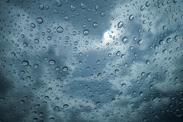 water drop of rain on a glass, blurred sun with blue sky and cloud, selective focus