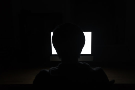 Silhouette of man using blank screen laptop in dark room