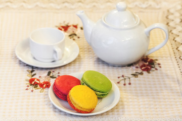 French colorful macarons on a plate, cup and teapot