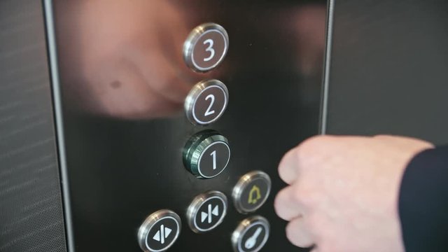 Close up of male hand pushing button on metal panel in the modern elevator