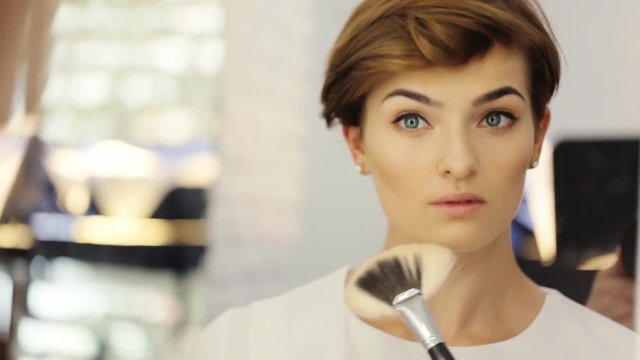 Beauty woman applying makeup. Beautiful girl looking in the mirror and applying cosmetic on the cheekbones with a big brush