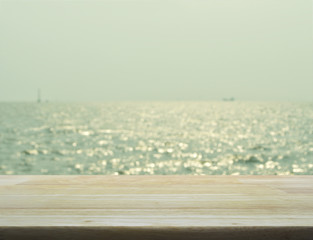 Empty wooden table with blurred sea waves with bokeh light, gree