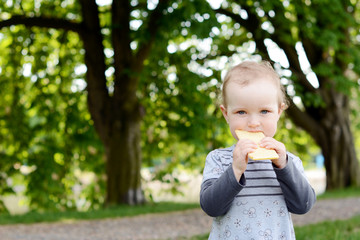 Little beautiful baby in the park eating peace of bread.