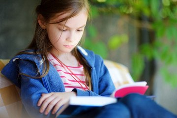 Cute little girl reading a book outdoors