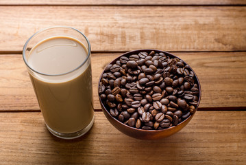 Coffee beans in bowl and a glass of coffee milk on wooden table.
