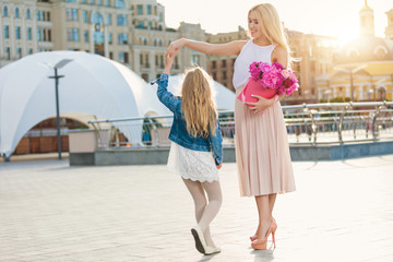 Portrait of young beautiful mother and daughter with box of peonies posing in the city streets. Flower box and gift box. Bouquet of flowers in gift box. Birthday. March 8