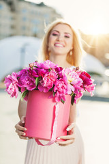 Portrait of young beautiful blonde woman with box of flowers posing in the city streets. flower box and gift box. bouquet of flowers in gift box. birthday, March 8, Valentine's Day, romantic