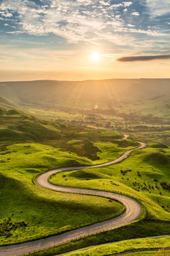 Winding country road leading to Edale in the English Peak District with beautiful golden light shining through valley.
