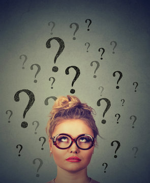 Thinking business woman with glasses looking up at many questions marks above head