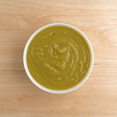Bowl of green pea soup on a wood table top view illuminated with natural light.