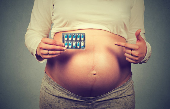 Closeup cropped image pregnant woman with big belly pointing at pills