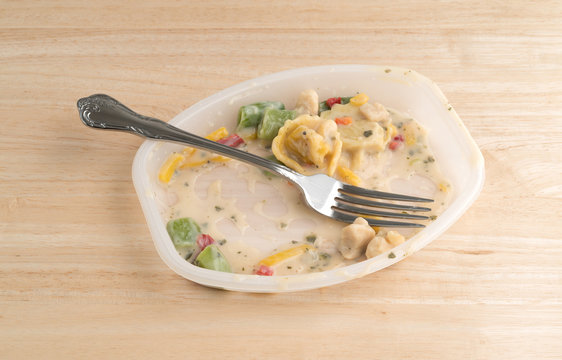 Partially eaten chicken tortellini TV dinner on a wood table with a fork in the tray.