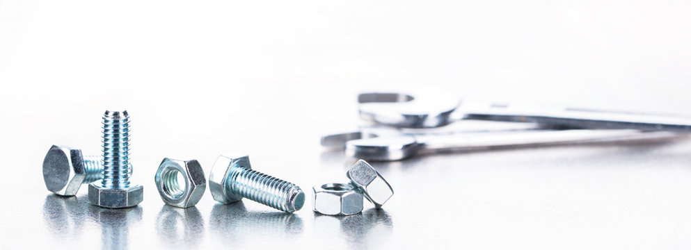 Schrauben, Muttern in Reihe und Schraubenschl&uuml;ssel auf spiegelnder Edelstahlplatte als Panorama