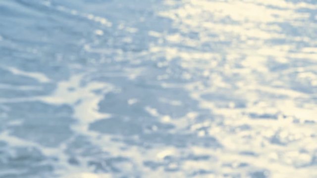 Sunlight sparkling on the water surface, waves rolling on a beach - slow motion - loop