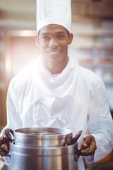 Smiling chef in kitchen holding cooking pot
