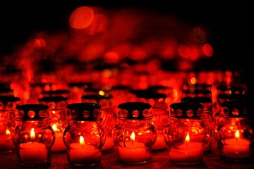 Many candles burning in red candle holders at night