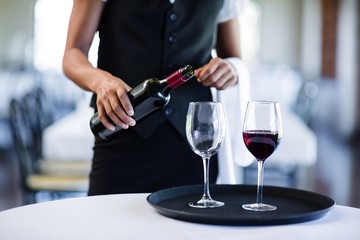 Mid section of waitress pouring red wine in a glass